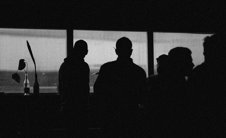 Grainy black-and-white scene of people gathered in silhouette by Mono Tape Club's windows.